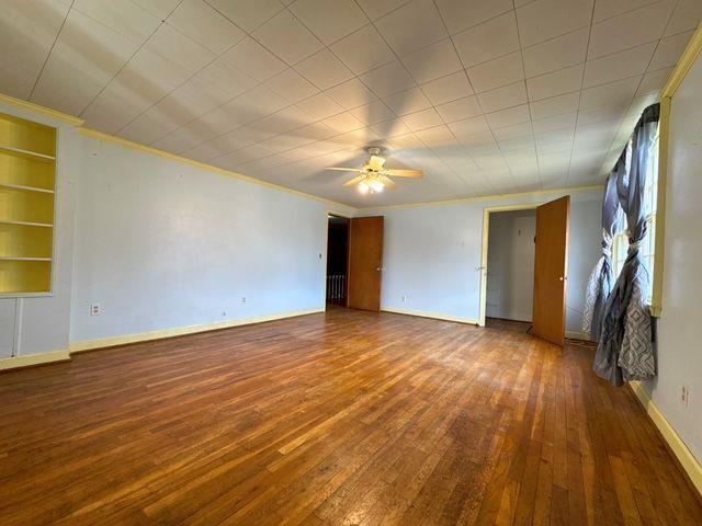 unfurnished room with wood-type flooring, ornamental molding, built in shelves, and ceiling fan