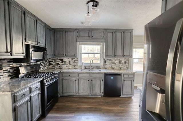 kitchen featuring plenty of natural light, decorative light fixtures, sink, black appliances, and light stone countertops