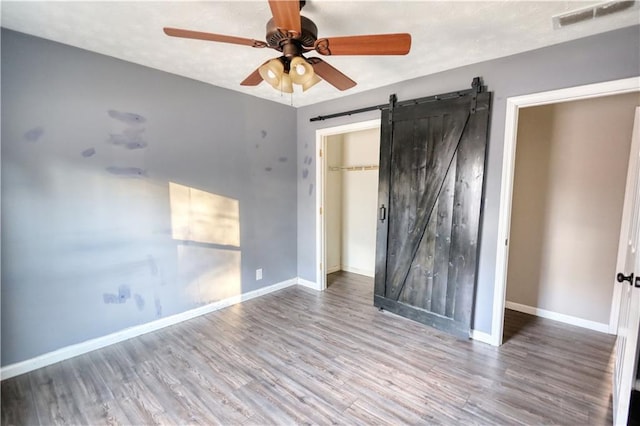 unfurnished bedroom with wood-type flooring, a barn door, ceiling fan, and a closet