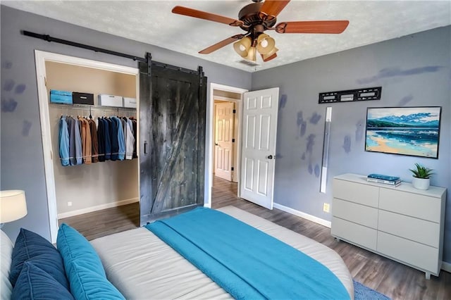 bedroom featuring ceiling fan, a textured ceiling, a barn door, dark hardwood / wood-style flooring, and a closet