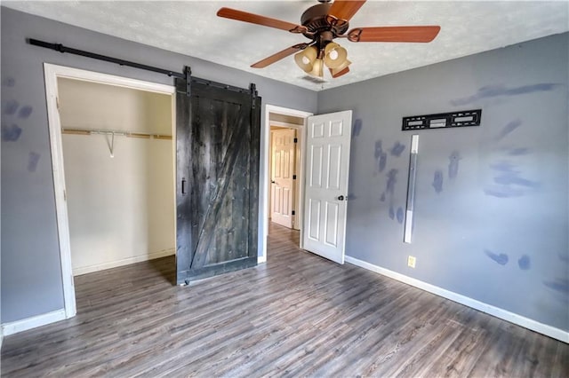 unfurnished bedroom with a barn door, hardwood / wood-style floors, ceiling fan, and a closet