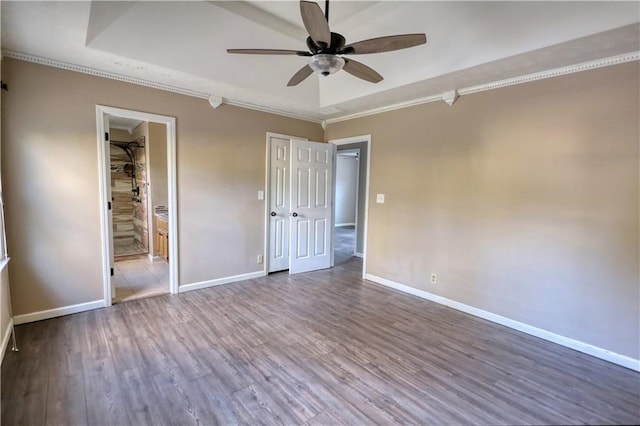 unfurnished bedroom with ensuite bath, wood-type flooring, ornamental molding, a raised ceiling, and ceiling fan