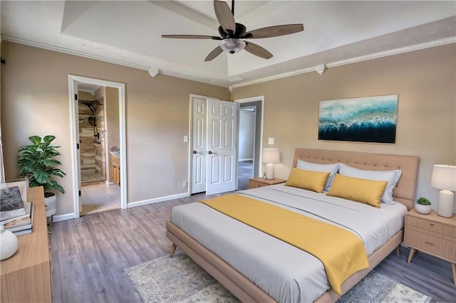 bedroom with connected bathroom, wood-type flooring, ornamental molding, ceiling fan, and a tray ceiling