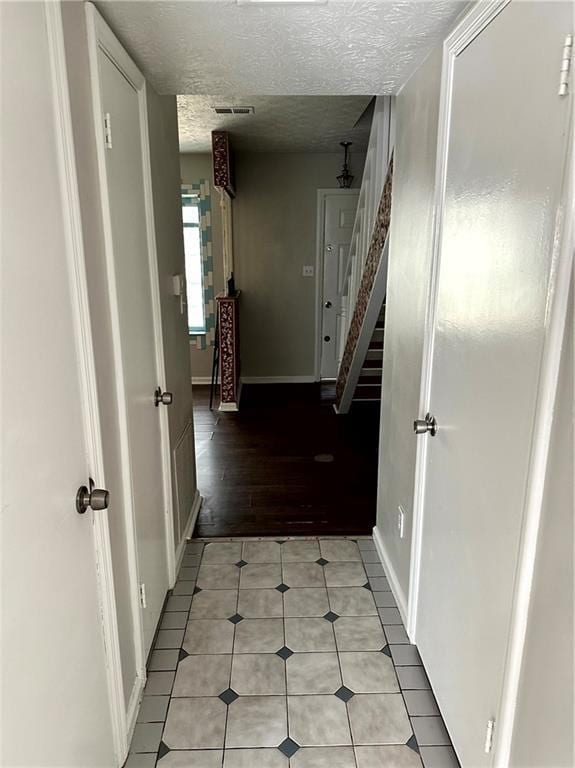 hallway with visible vents, baseboards, stairway, a textured ceiling, and light tile patterned floors