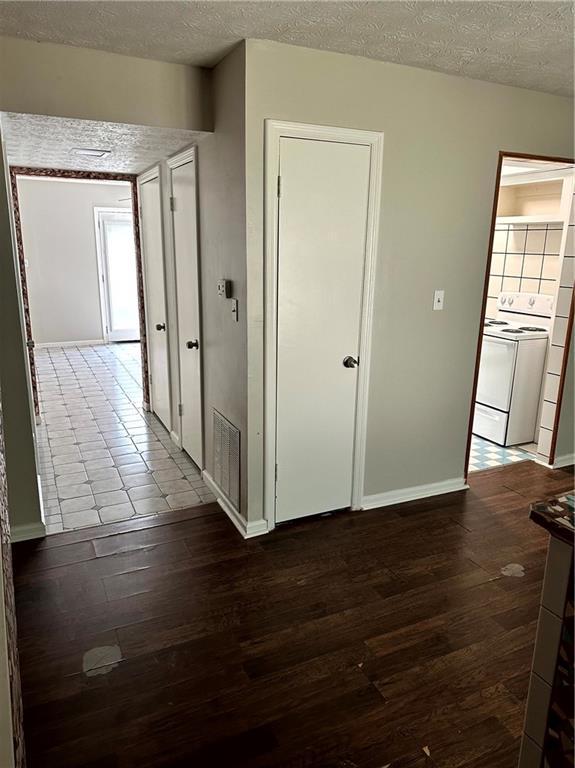 corridor featuring baseboards, dark wood-style flooring, a textured ceiling, and visible vents