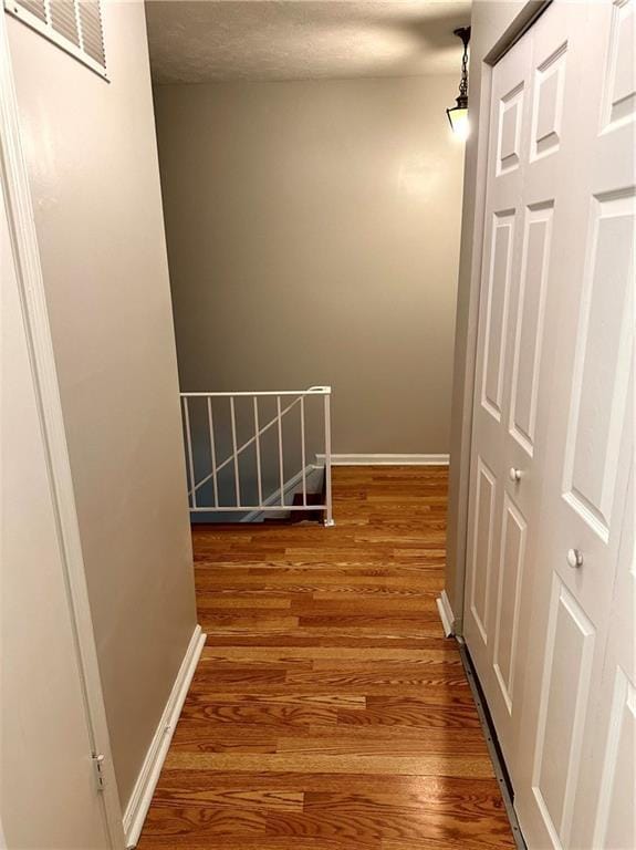 corridor with baseboards, an upstairs landing, wood finished floors, and visible vents