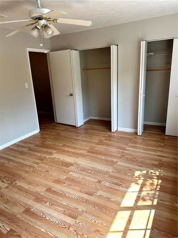 unfurnished bedroom with baseboards, a ceiling fan, two closets, and light wood-type flooring