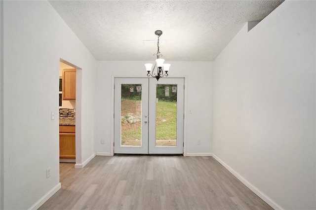 unfurnished dining area with an inviting chandelier, light hardwood / wood-style floors, french doors, and a textured ceiling