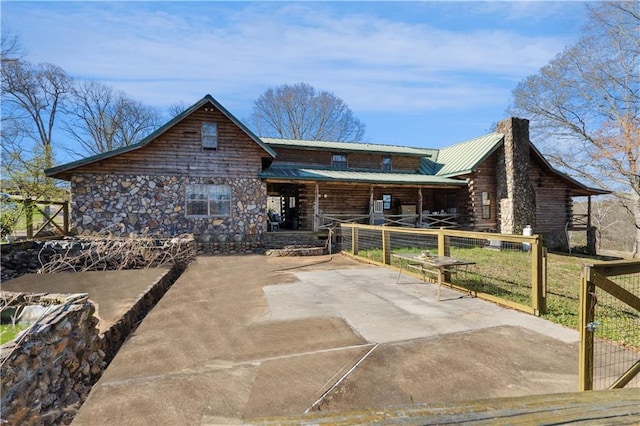 cabin with log exterior, metal roof, a chimney, and fence