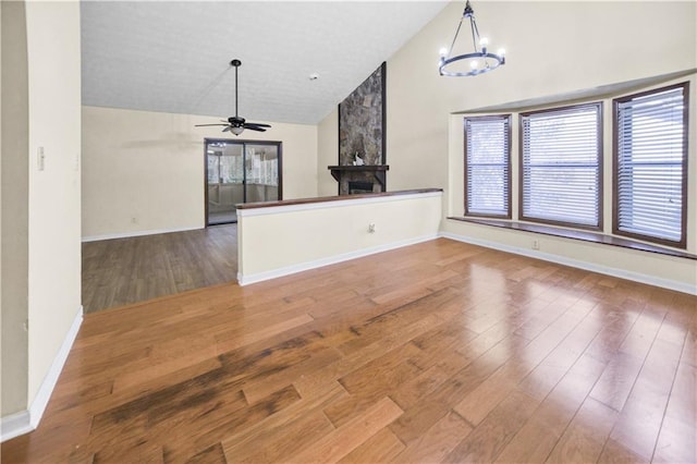 unfurnished living room with ceiling fan with notable chandelier, high vaulted ceiling, a stone fireplace, and hardwood / wood-style floors