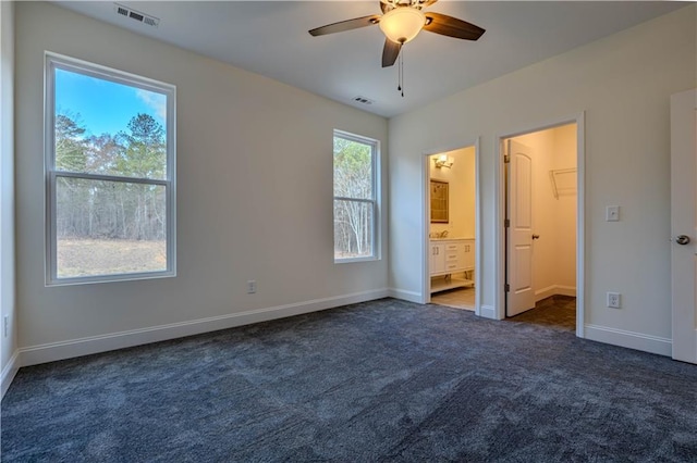 unfurnished bedroom with ensuite bathroom, ceiling fan, and dark carpet