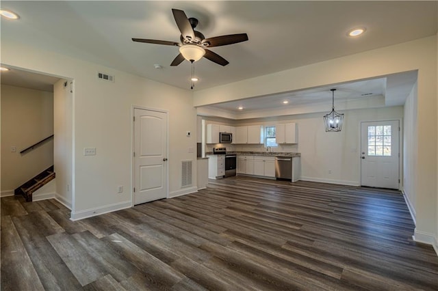 unfurnished living room with dark hardwood / wood-style floors, ceiling fan with notable chandelier, and a tray ceiling