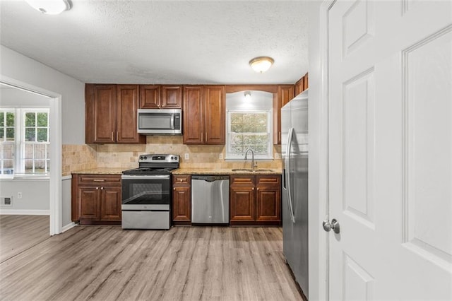 kitchen with stainless steel appliances, light hardwood / wood-style flooring, sink, light stone countertops, and a textured ceiling