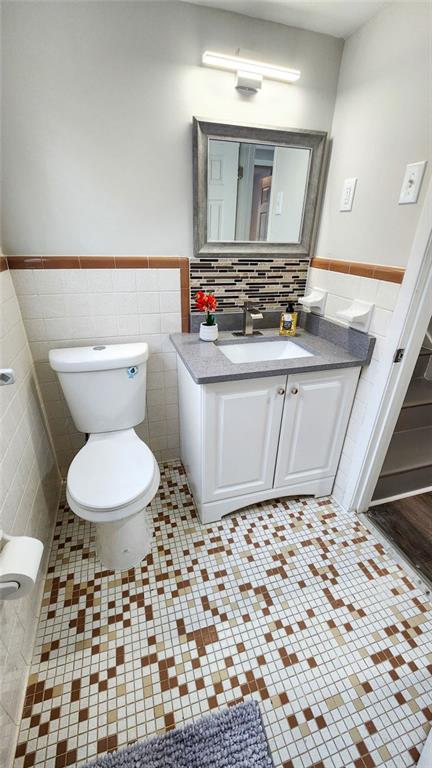 bathroom featuring tile walls, a wainscoted wall, vanity, and toilet