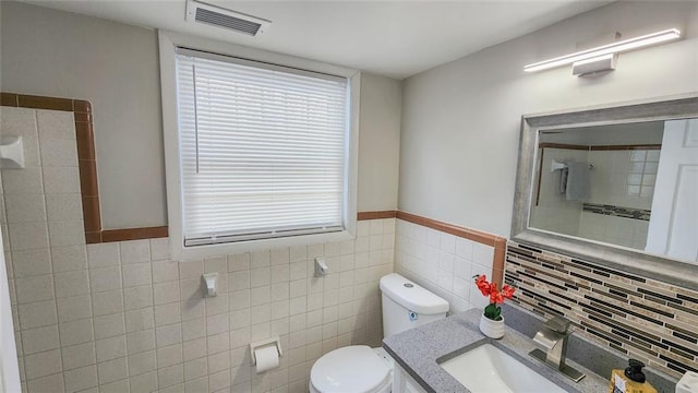 full bathroom with toilet, a tile shower, visible vents, and tile walls