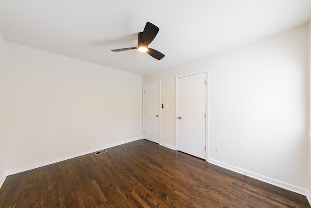 spare room with dark wood-style floors, visible vents, ceiling fan, and baseboards