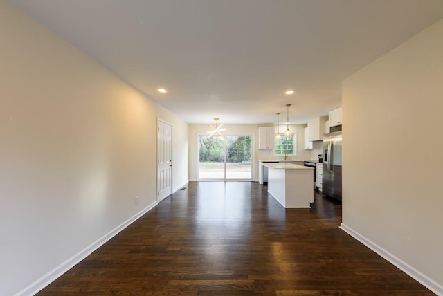 unfurnished living room with baseboards, recessed lighting, dark wood-style flooring, a sink, and a notable chandelier