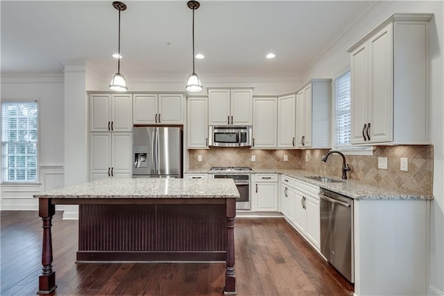 kitchen with pendant lighting, sink, stainless steel appliances, a center island, and light stone countertops