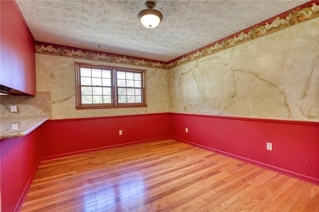 empty room with light wood-type flooring and a textured ceiling