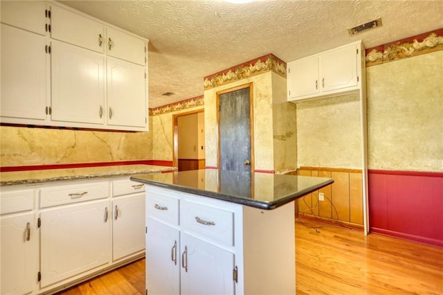 kitchen featuring a center island, light wood-type flooring, a textured ceiling, and white cabinetry