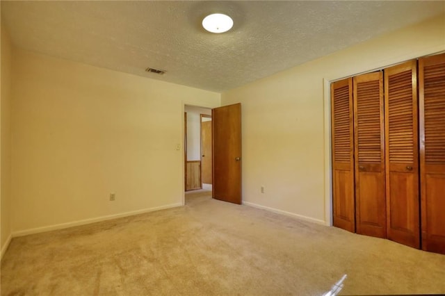 unfurnished bedroom featuring light carpet, a closet, and a textured ceiling