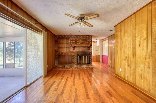 unfurnished living room featuring wood walls, light hardwood / wood-style floors, and a textured ceiling