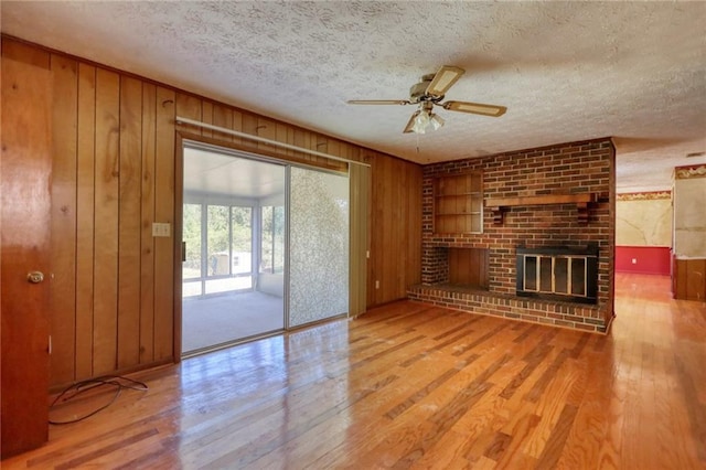 unfurnished living room featuring a fireplace, wooden walls, light hardwood / wood-style flooring, and a textured ceiling