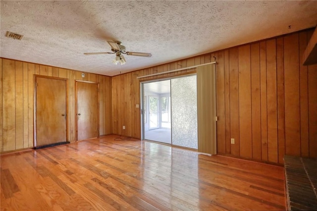 interior space with hardwood / wood-style floors, ceiling fan, wood walls, and a textured ceiling