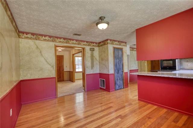 kitchen with kitchen peninsula, a textured ceiling, and light hardwood / wood-style flooring