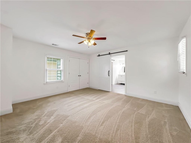 644 Albert St NW, Atlanta, GA 30318 - unfurnished bedroom with a barn door, light carpet, a closet, ceiling fan, and connected bathroom