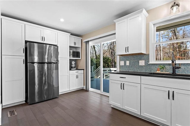 kitchen with dark wood-type flooring, a sink, dark countertops, backsplash, and stainless steel appliances