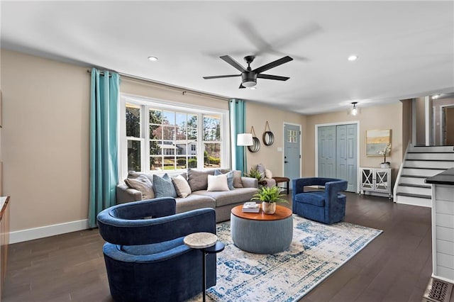 living area with baseboards, a ceiling fan, dark wood-style flooring, and stairs