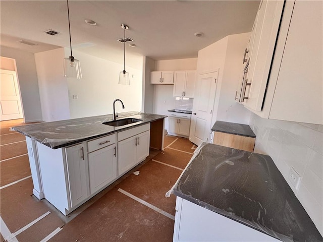 kitchen with sink, white cabinetry, a center island with sink, dark stone countertops, and pendant lighting