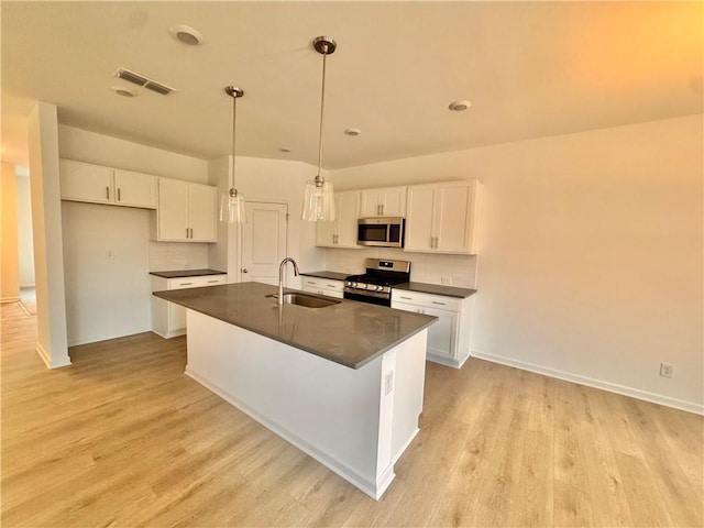 kitchen with dark countertops, visible vents, appliances with stainless steel finishes, white cabinets, and a sink