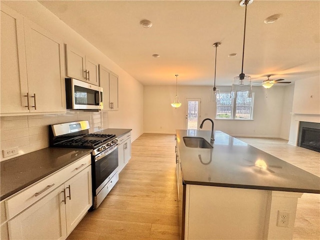 kitchen featuring light wood finished floors, dark countertops, decorative backsplash, appliances with stainless steel finishes, and a sink