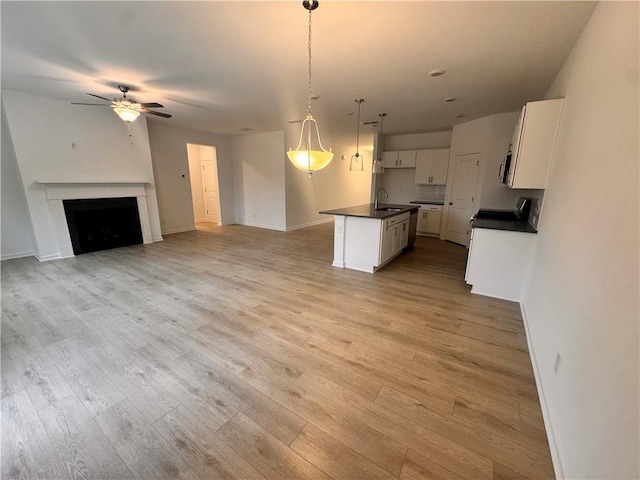 kitchen with dark countertops, ceiling fan, open floor plan, light wood-style floors, and white cabinetry