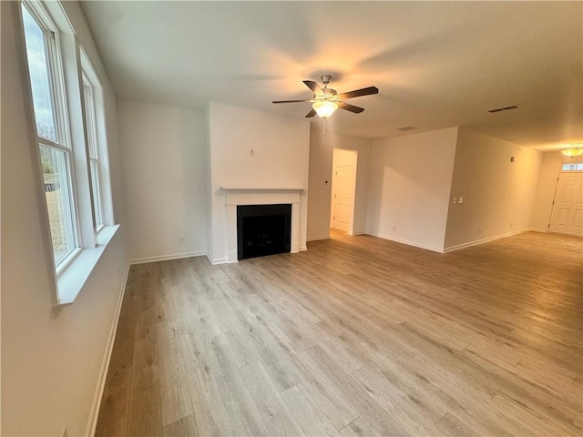 unfurnished living room with a fireplace, light wood finished floors, visible vents, ceiling fan, and baseboards