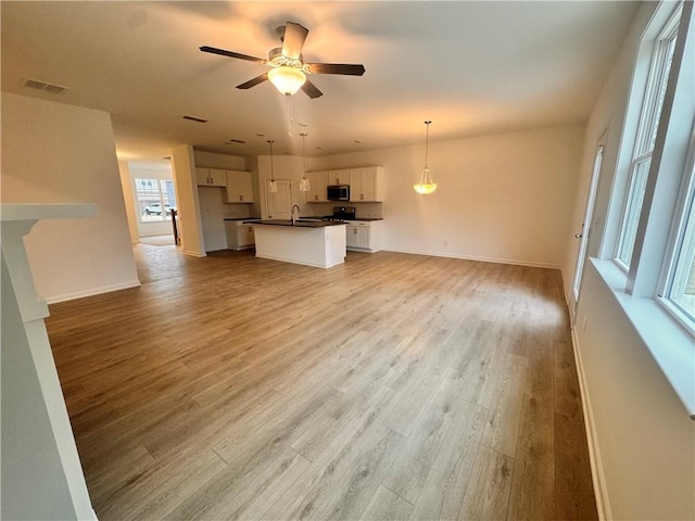 unfurnished living room featuring light wood-style floors, baseboards, visible vents, and a ceiling fan