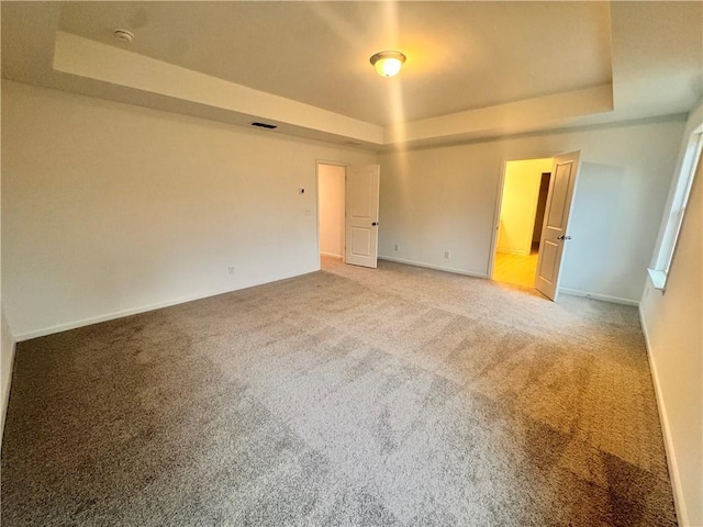 unfurnished room featuring a tray ceiling, carpet, and baseboards