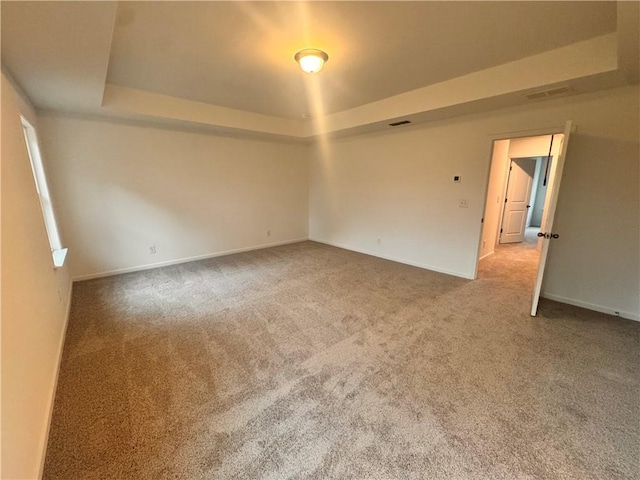 carpeted empty room with visible vents, baseboards, and a raised ceiling