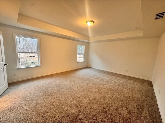 carpeted spare room featuring baseboards, visible vents, and a raised ceiling