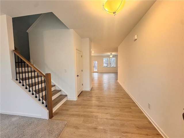 hallway featuring stairway, light wood-style flooring, and baseboards