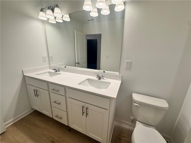 bathroom with toilet, double vanity, a sink, and wood finished floors