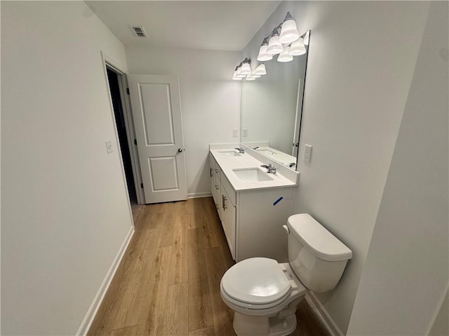 bathroom featuring visible vents, toilet, vanity, wood finished floors, and baseboards