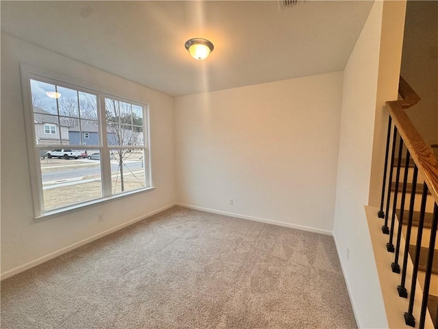 carpeted empty room featuring stairway and baseboards