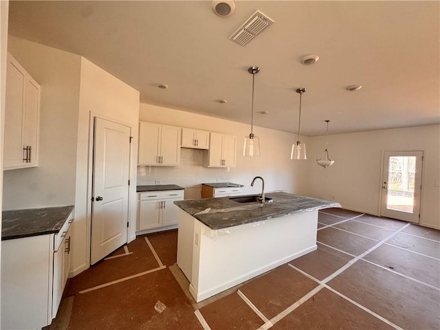 kitchen featuring sink, white cabinets, decorative backsplash, hanging light fixtures, and a kitchen island with sink