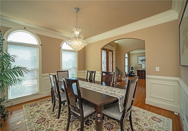 dining space with arched walkways, wainscoting, crown molding, and wood finished floors