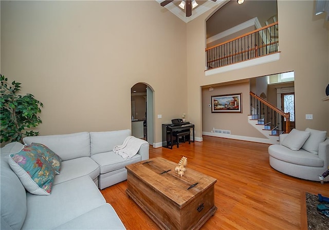 living room with arched walkways, visible vents, light wood-type flooring, baseboards, and stairs