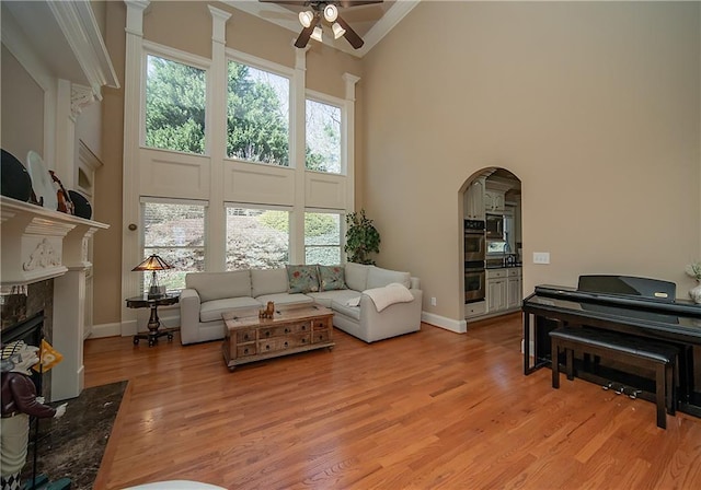 living area with light wood finished floors, baseboards, arched walkways, a towering ceiling, and a fireplace