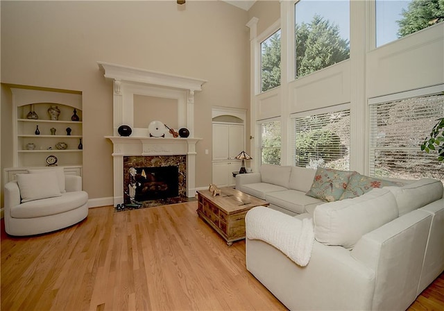 living area with light wood finished floors, baseboards, a towering ceiling, built in shelves, and a fireplace